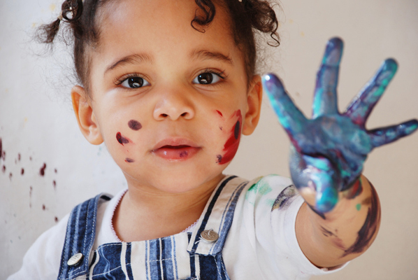 A child has been finger painting and is covered in paint, representing the spread of germs.